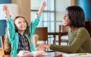 Tutor smiling at student that is celebrating with hands in the air